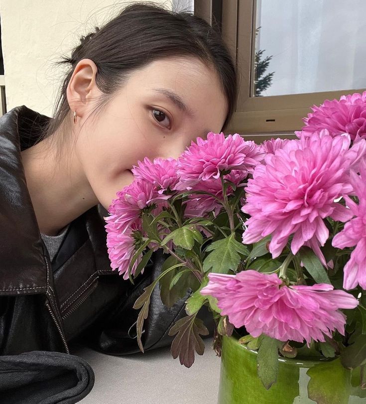 a woman leaning over a vase with pink flowers in it and looking at the camera