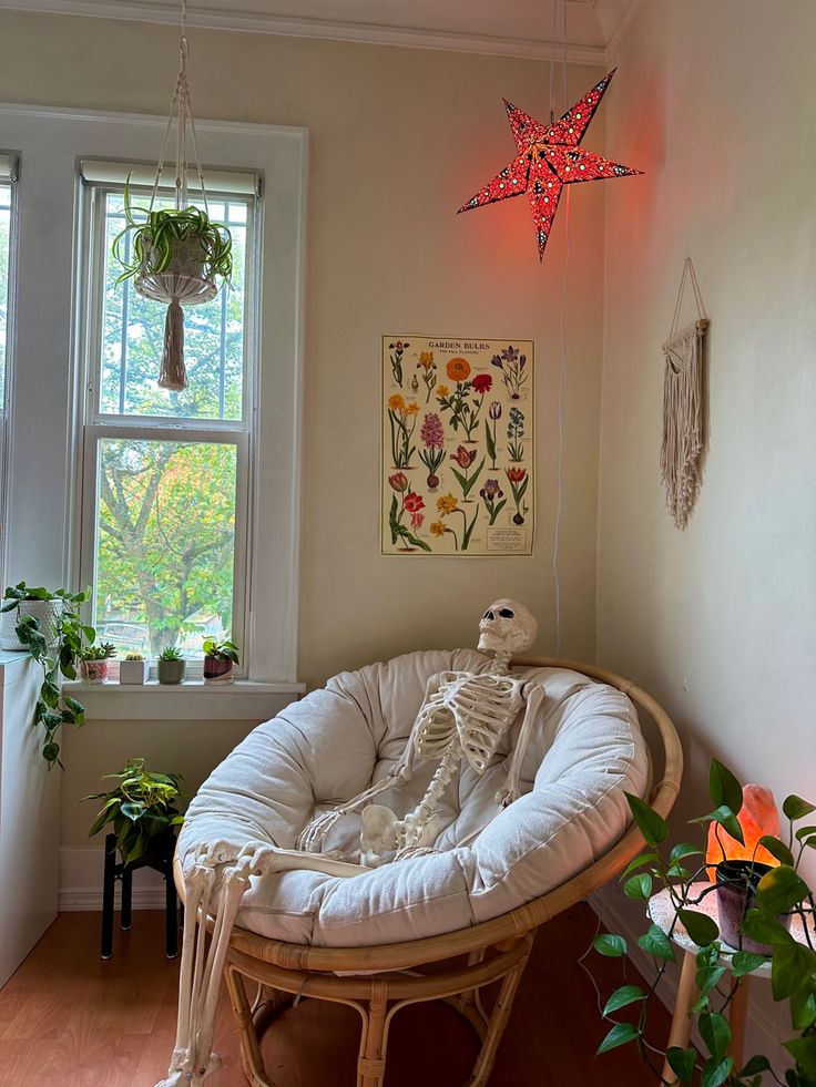 a skeleton sitting on a chair in front of a window next to a potted plant