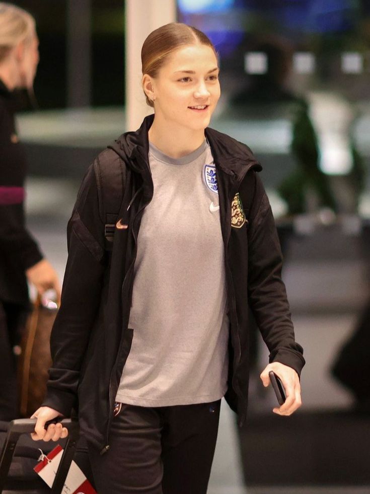 a woman walking through an airport with her hand in her pocket and luggage behind her