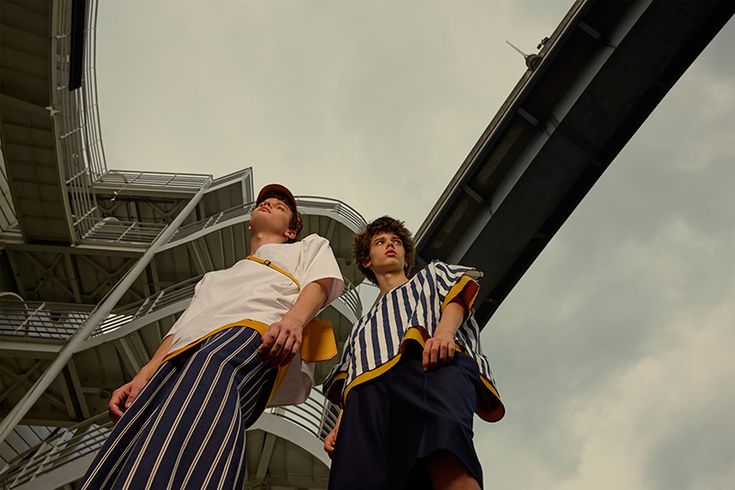 two men standing next to each other in front of a tall building with a sky background