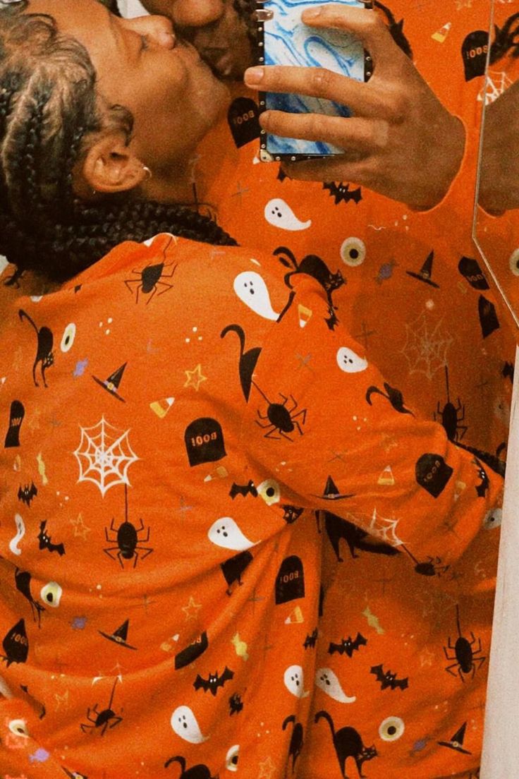 a woman in an orange pajamas taking a selfie with her cell phone while she is dressed up for halloween