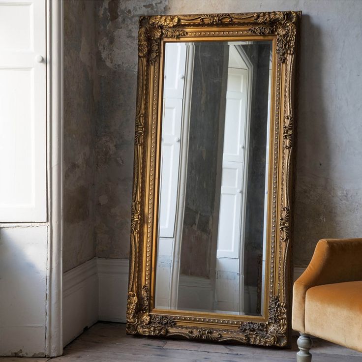 a large gold framed mirror sitting on top of a wooden floor next to a chair