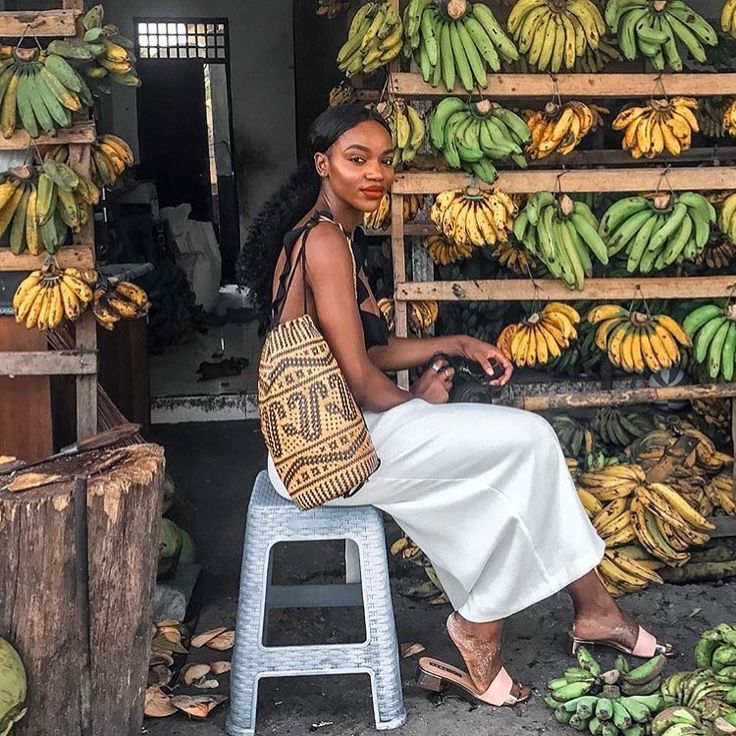 a woman sitting on a stool next to bunches of bananas