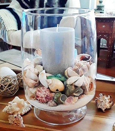 a glass vase filled with seashells and a lit candle on top of a wooden table