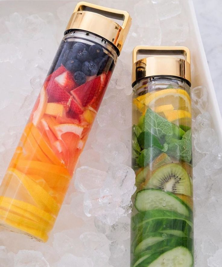 two glass bottles filled with different types of fruits and veggies on top of ice