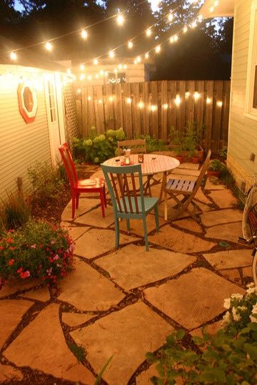 an outdoor patio with lights strung over it and chairs around the table in the middle