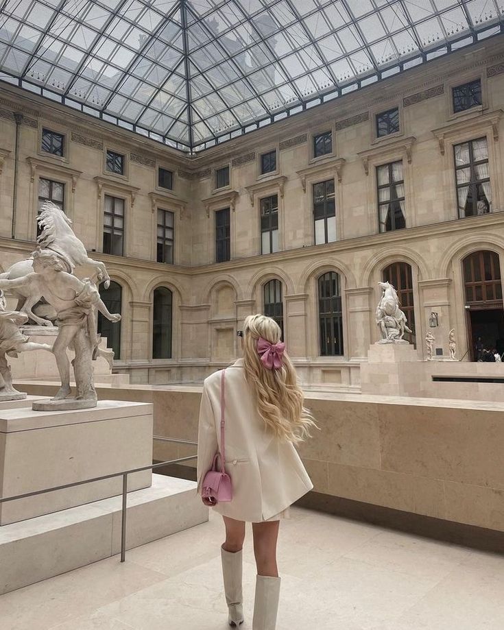 a woman standing in front of a building with a horse statue on the other side