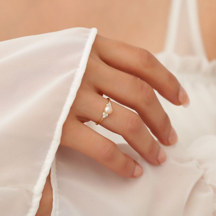 a woman's hand wearing a gold ring with pearls on the band and a white dress