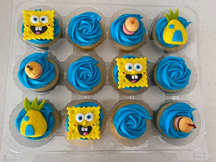 cupcakes with blue frosting and yellow decorations are arranged in a plastic container