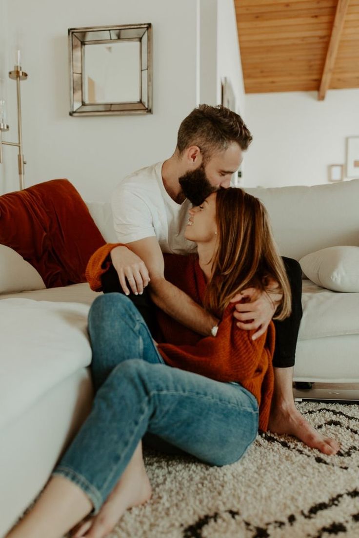 a man and woman sitting on the floor in front of a couch with their arms around each other