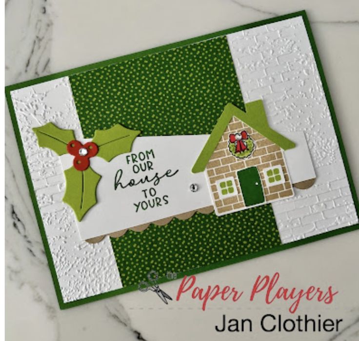 a close up of a card with a house and holly decoration on the front,