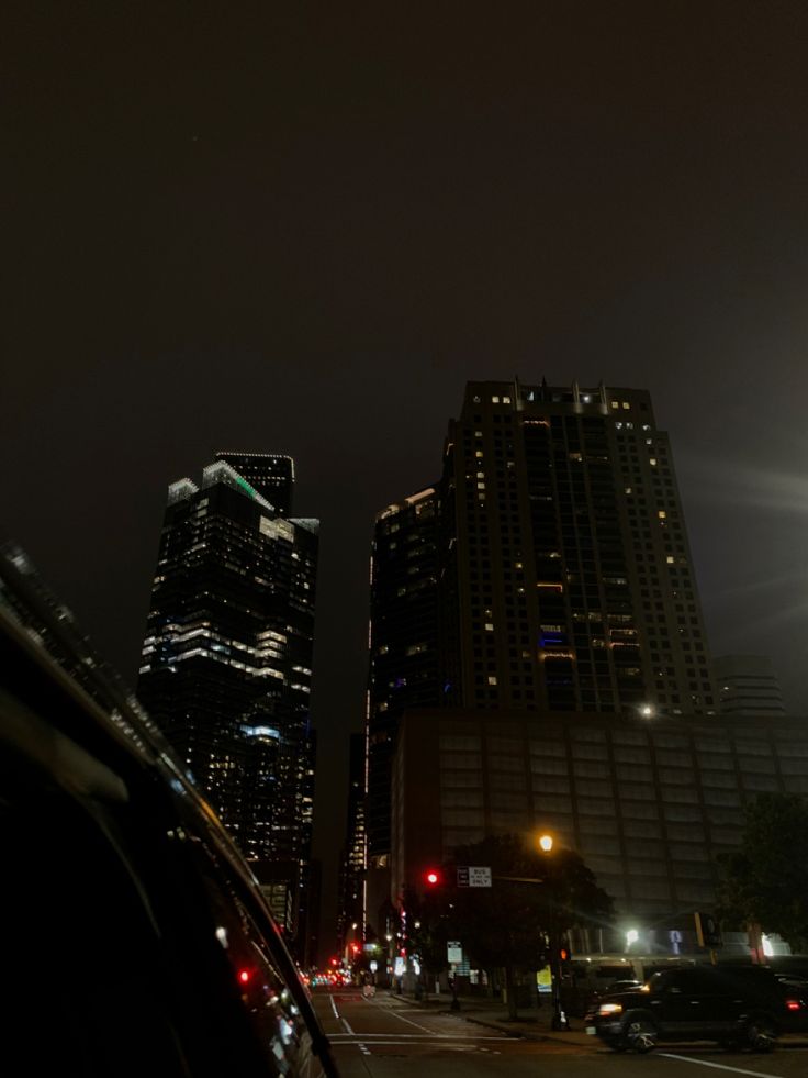 a city street at night with tall buildings in the background