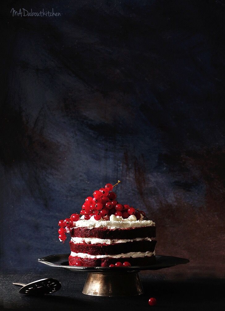 a red and white cake on a black plate with cherries around the edges, next to a pair of scissors