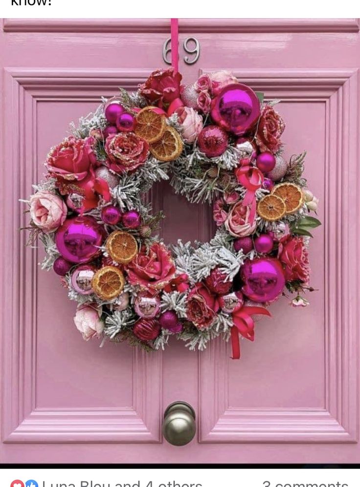 a pink door with a wreath hanging on it's side and an orange slice in the middle