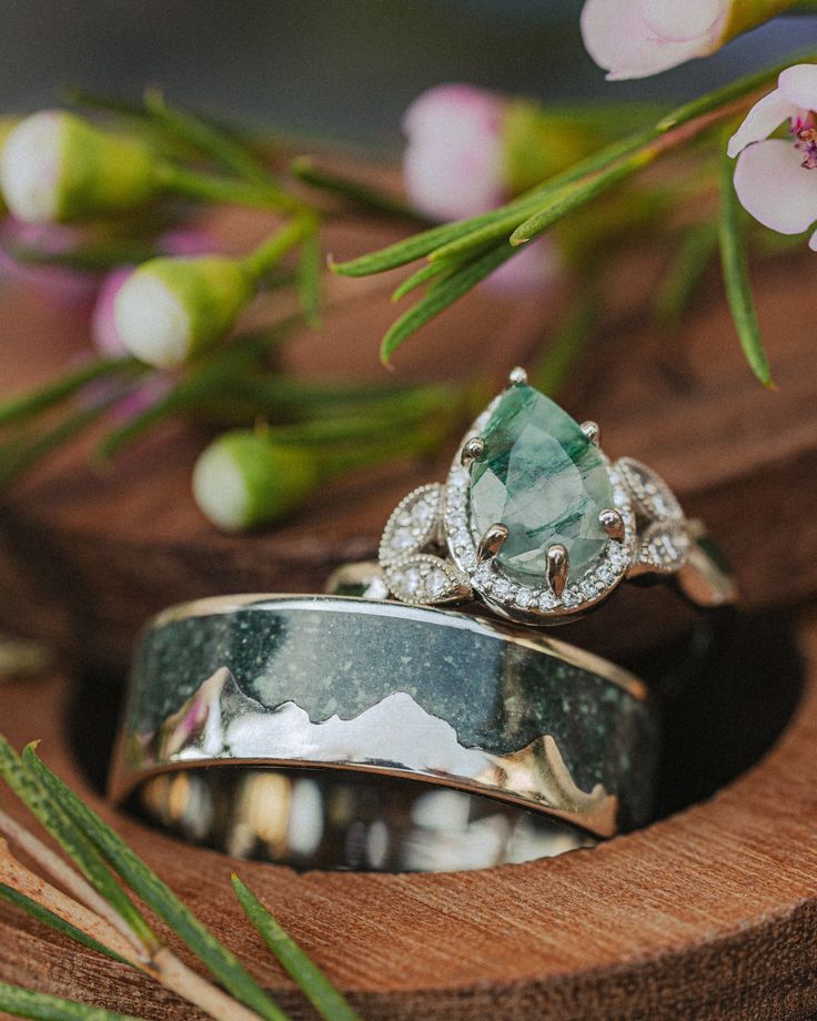 two wedding rings sitting next to each other on top of a wooden stand with flowers in the background