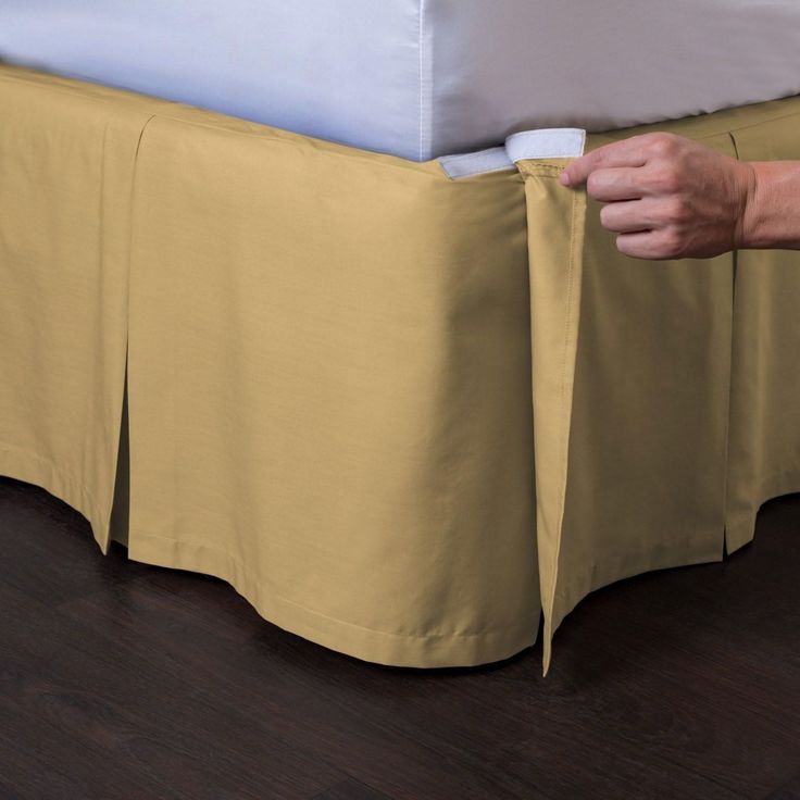 a person is holding onto the edge of a bed with a yellow skirt on it