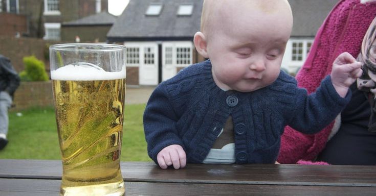 a baby sitting at a table next to a glass of beer