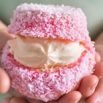 a person holding a pink donut with white frosting and sprinkles