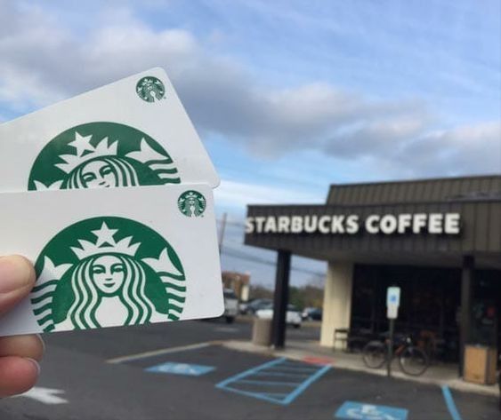 a person holding up two starbucks stickers in front of a starbucks coffee shop building