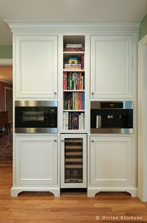 a kitchen with white cabinets and wood flooring in front of an open bookcase