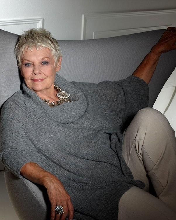 an older woman sitting in a chair with her legs crossed and wearing a gray sweater