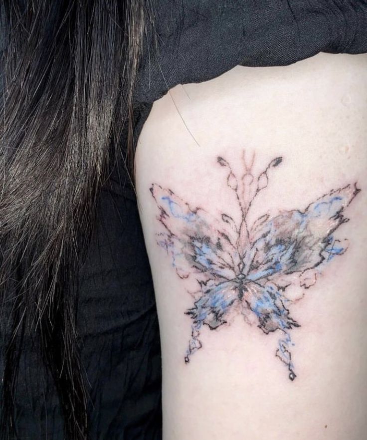 the back of a woman's shoulder with a blue and black butterfly tattoo on it