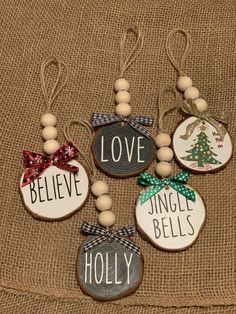 christmas ornaments with words and bows are hanging on a burlap cloth covered surface