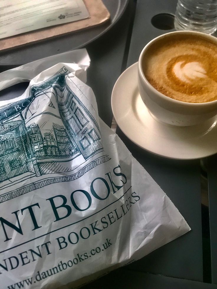 a cup of coffee sitting on top of a table next to a bag of books