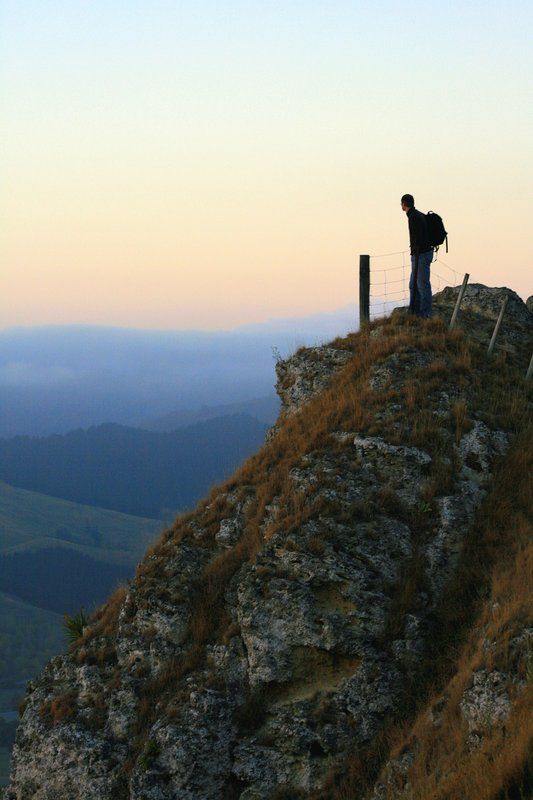 a man standing on top of a hill next to a fence and grass covered hillside