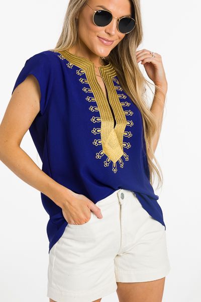 a woman wearing white shorts and a blue top with gold embroidery on the neckline