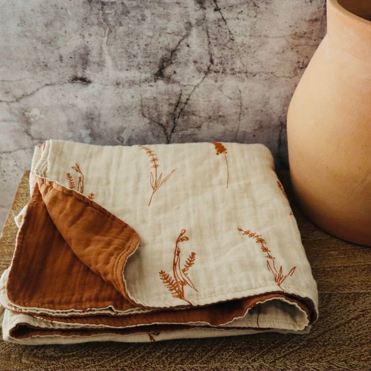 a brown vase sitting on top of a wooden table next to a white and tan cloth