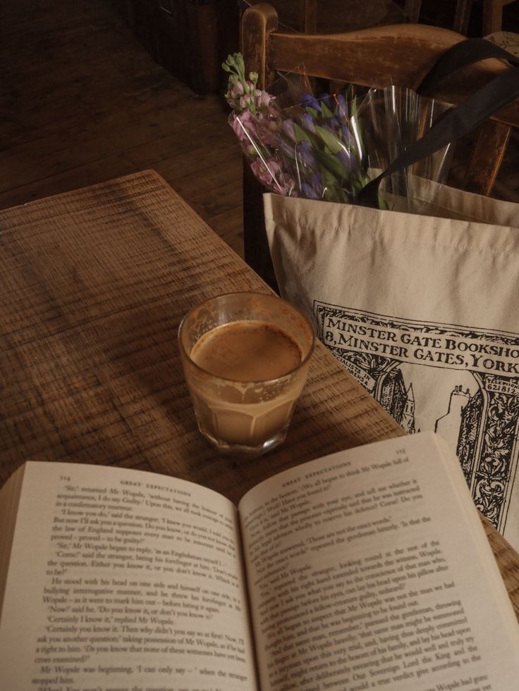 an open book sitting on top of a wooden table next to a cup of coffee