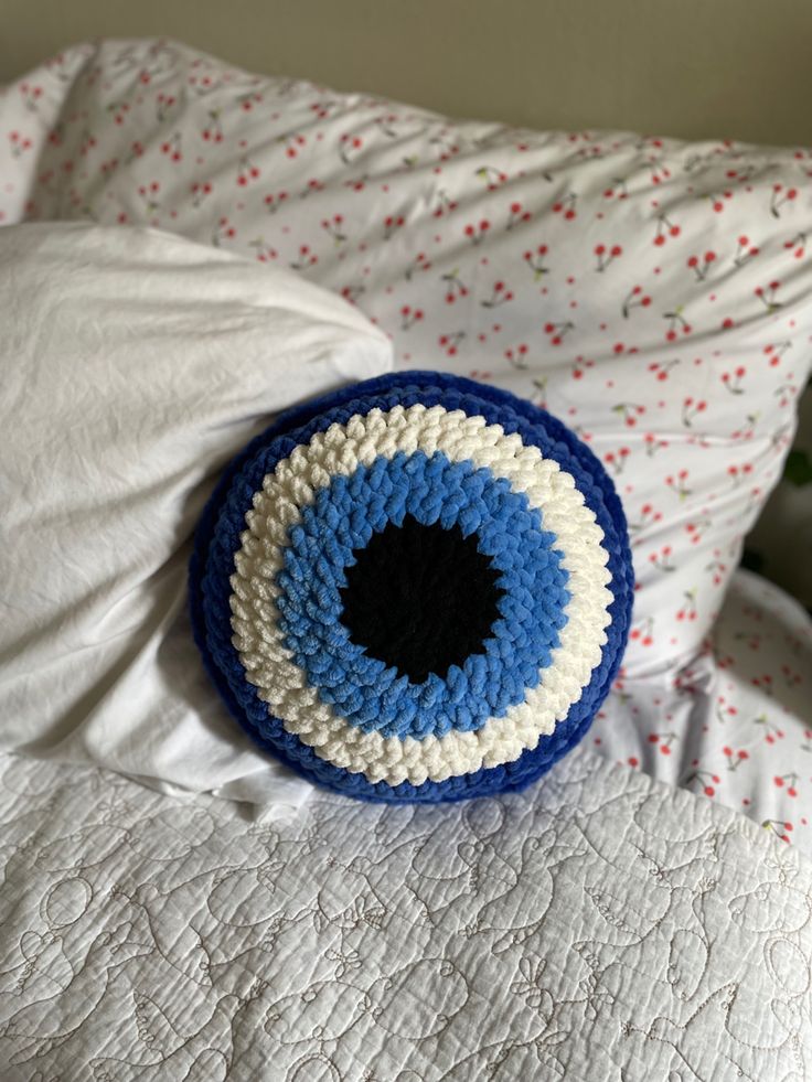 a crocheted blue and white eyeball pillow on a bed