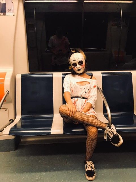 a woman with makeup and face paint sitting on a bus seat wearing fishnet stockings