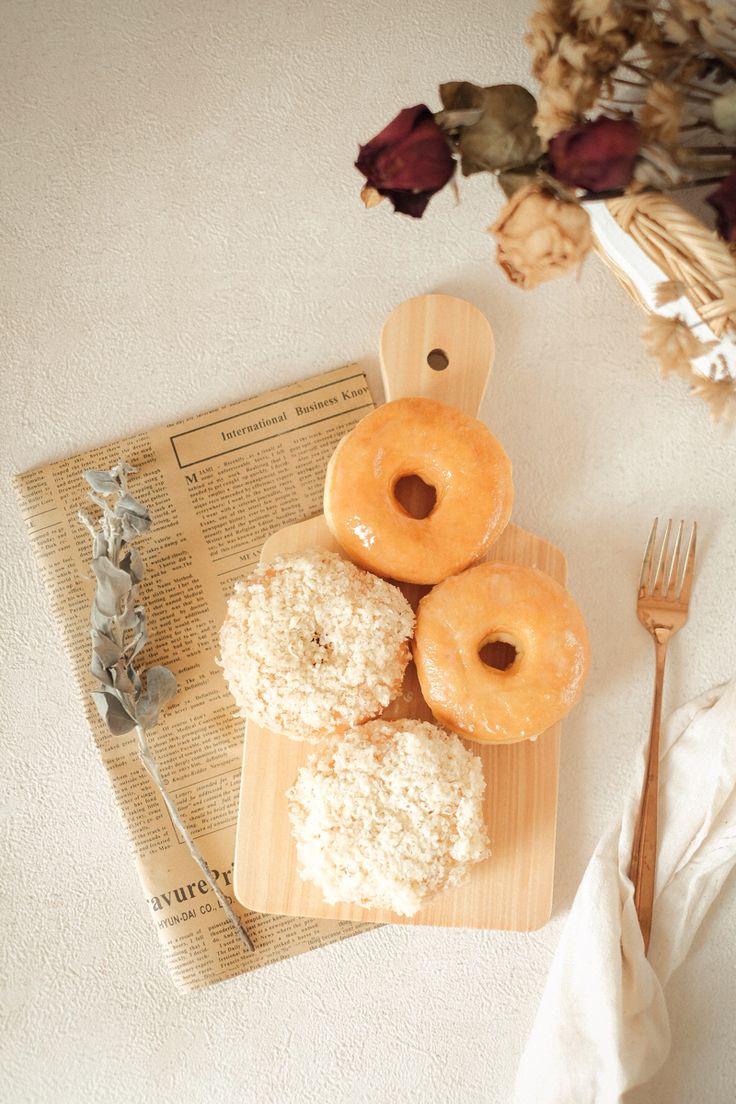 three donuts sitting on top of a wooden cutting board next to a knife and fork