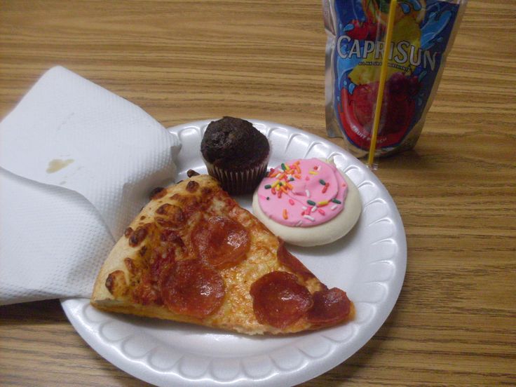 a slice of pizza on a paper plate with cupcakes and an ice cream sundae