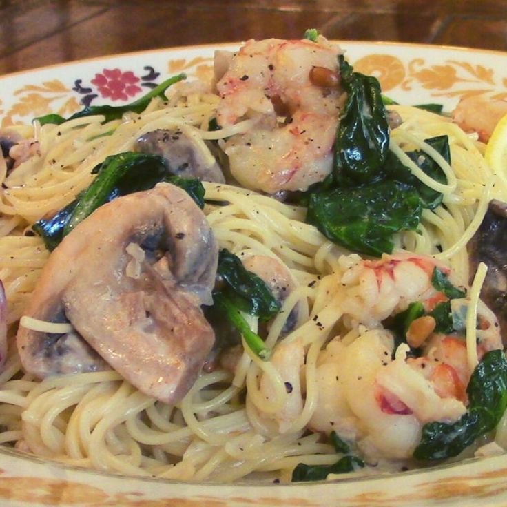 a pasta dish with shrimp, spinach and mushrooms on a yellow and white plate