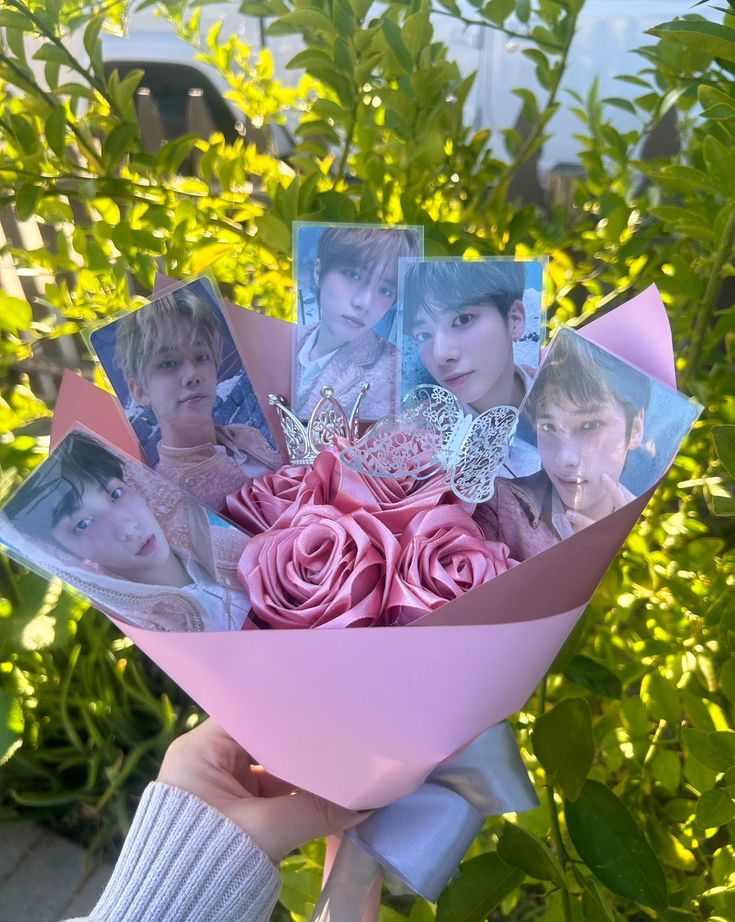 a person holding a bunch of flowers with pictures on it in front of some bushes