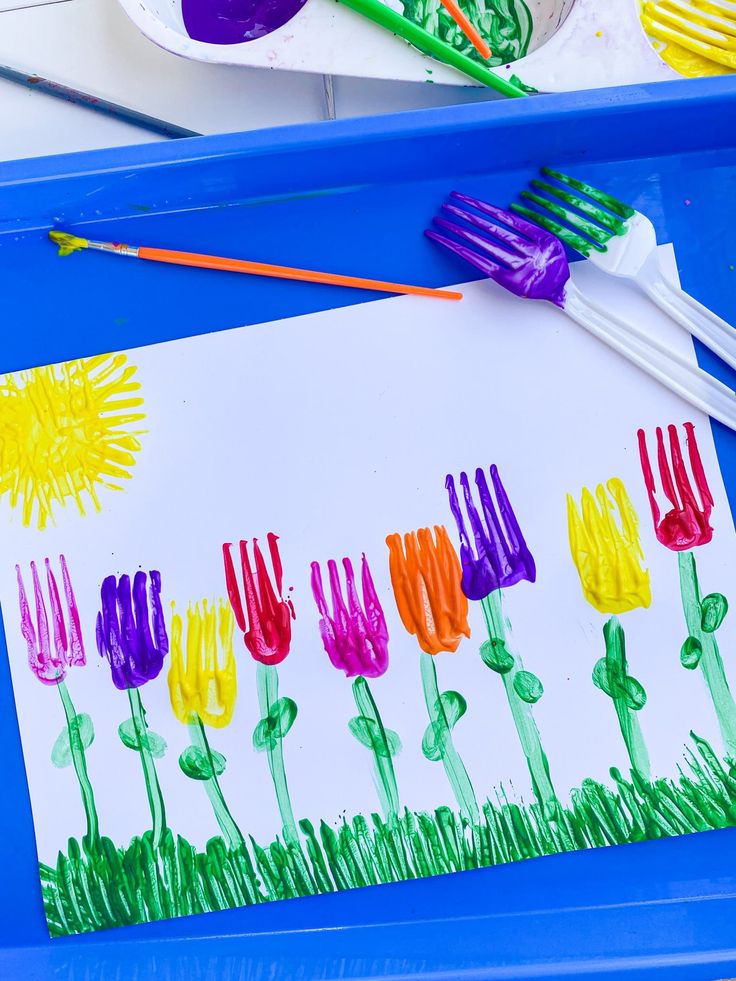 a child's art project with flowers painted on paper and paintbrushes in the background