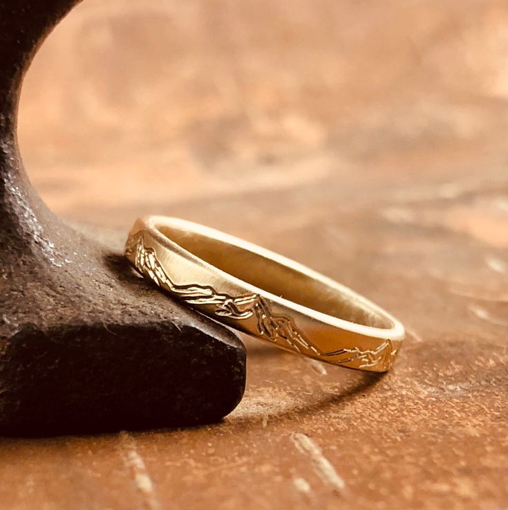 two gold wedding rings sitting on top of a wooden table next to a black piece of wood