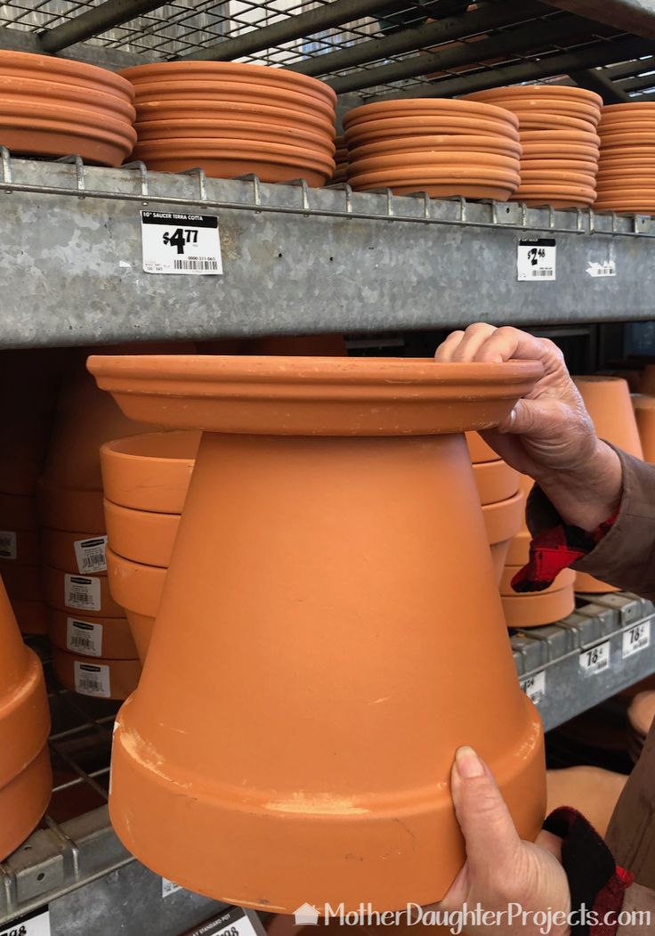 a person is holding a clay pot in front of some shelves with other clay pots