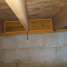 an unfinished ceiling with two square yellow bars hanging from it's sides and some wood planks on the floor