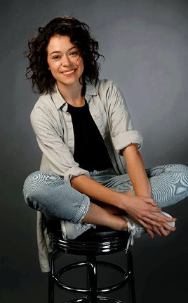 a woman sitting on top of a stool smiling at the camera with her legs crossed