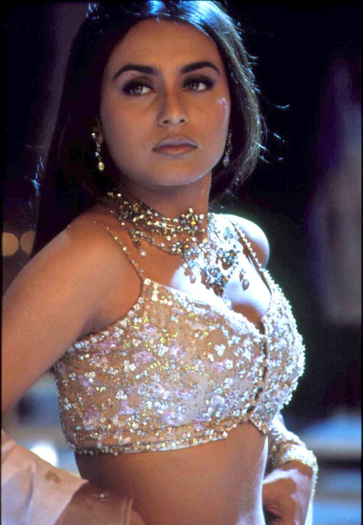 a woman in a gold and white outfit with jewels on her chest, posing for the camera