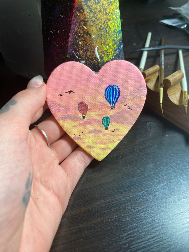 a hand holding a painted heart with hot air balloons on it