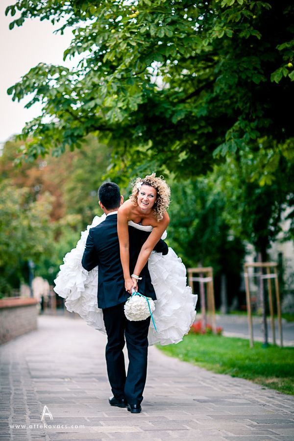 a bride carrying her groom down the street in their wedding day dress and tuxedo