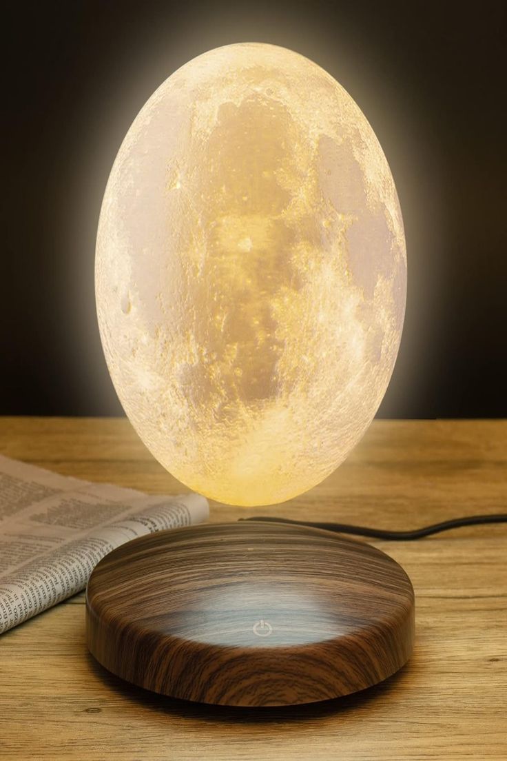 the moon lamp is sitting on top of a wooden table next to an open book