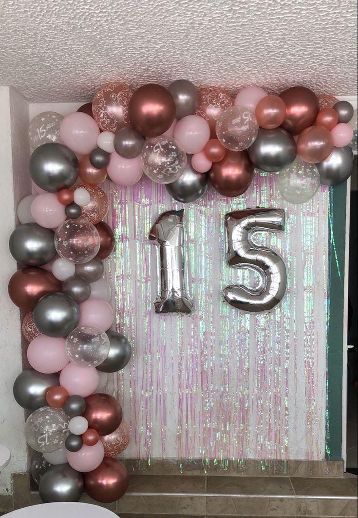 the number fifteen is surrounded by balloons and streamers in pink, silver and rose colors