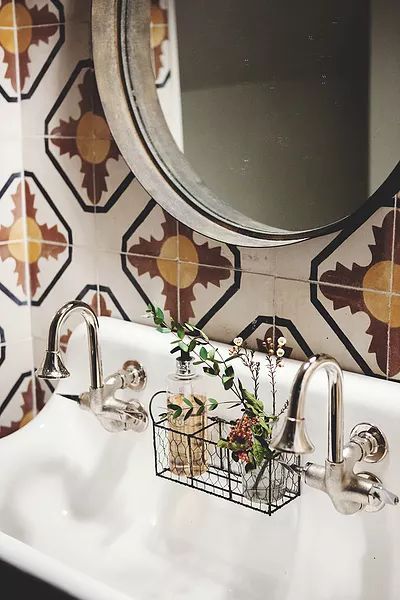 a white sink sitting under a mirror next to a metal basket filled with flowers and plants