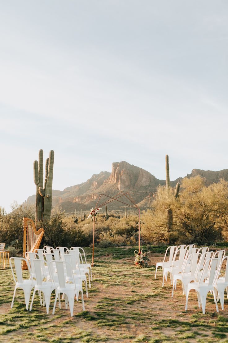 white chairs are set up for an outdoor ceremony in the desert with mountains in the background